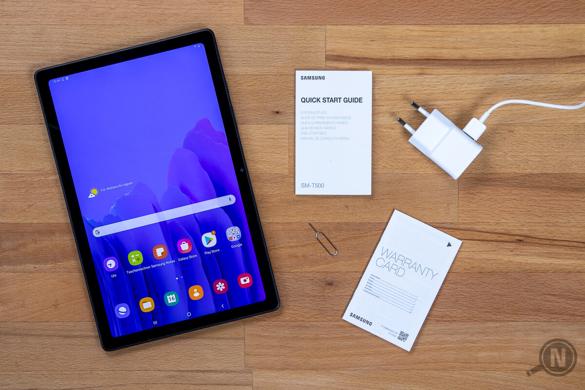 Links eingeschaltetets Samsung Galaxy Tab A7, rechts davon Quick Start Guid, SIM-Tool, Warranty-Card und Netzteil