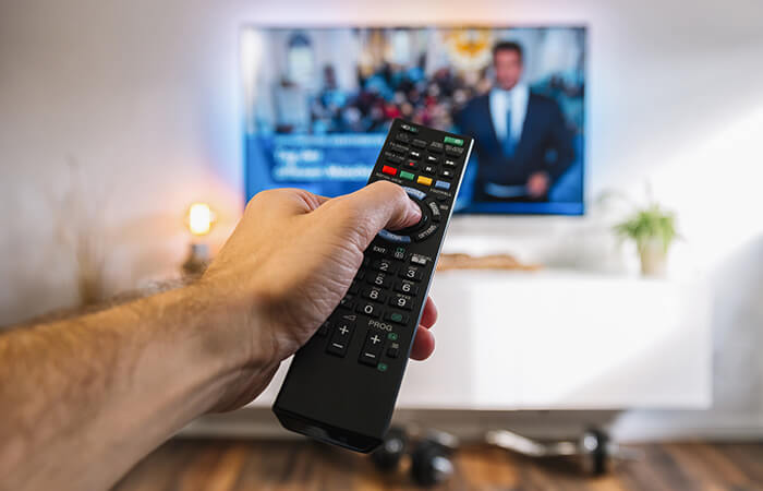 hand mit fernbedienun gfür fernseher im hintergrund