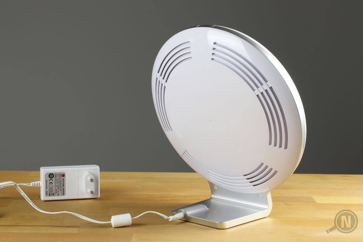 Die Rückseite einer auf einem Tisch stehenden Tageslichtlampe; das Netzteil liegt links daneben.
