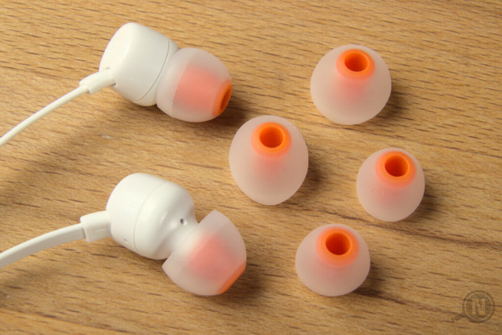 Großaufnahme von weiß-orangen In-Ear-Kopfhörern mit zwei Paar Ersatz-Ohrstöpseln in verschiedenen Größen