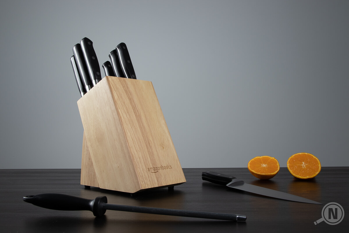 Messerblock auf schwarzem Tisch, ein Wetzstahl, ein Küchenmesser und eine aufgeschnittene Orange liegen um ihn herum.