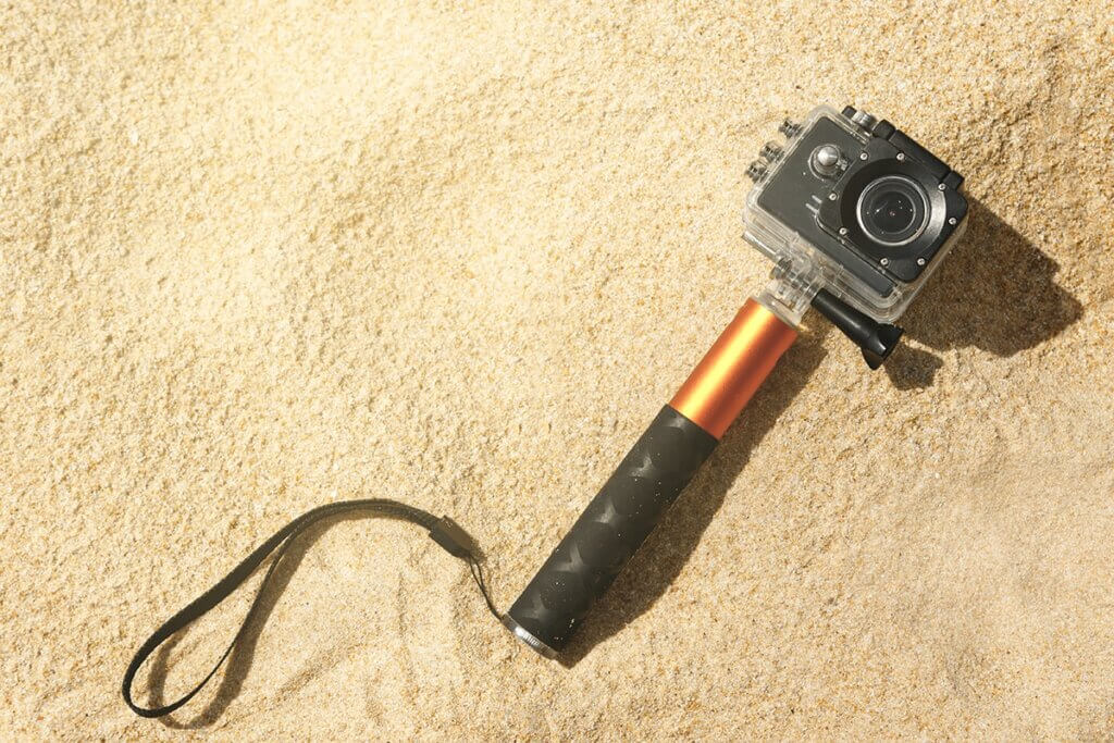 Action-Cam mit Stab liegt im Sand