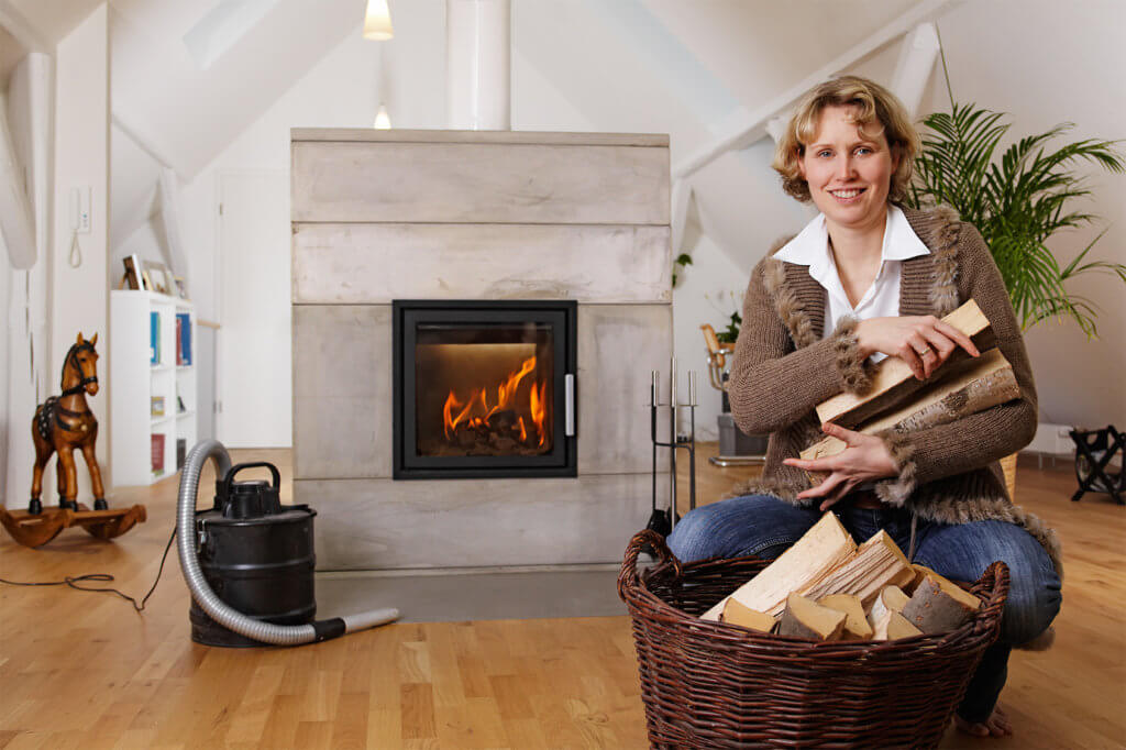 Frau mit Holz auf dem Arm, Aschesauger im Hintergrund