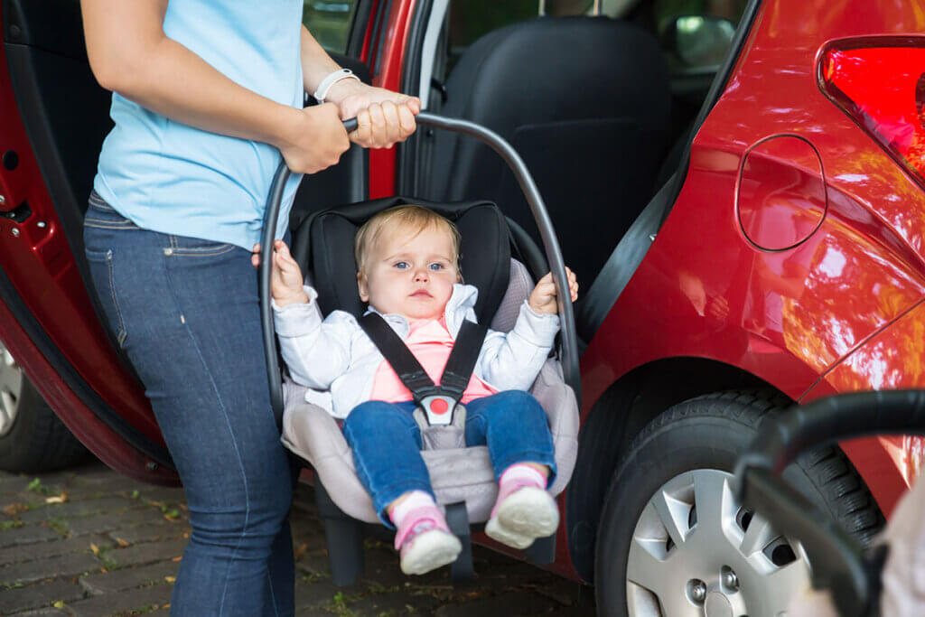 Person hält babyschale mit Baby vor einem Auto mit geöffneter Tür