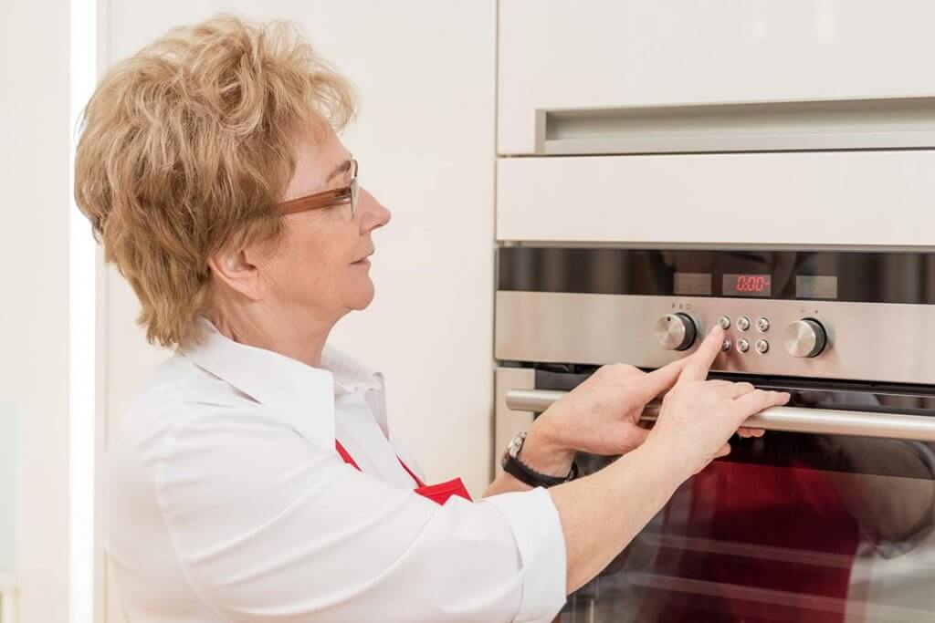 aeltere frau stellt ofen in kueche ein