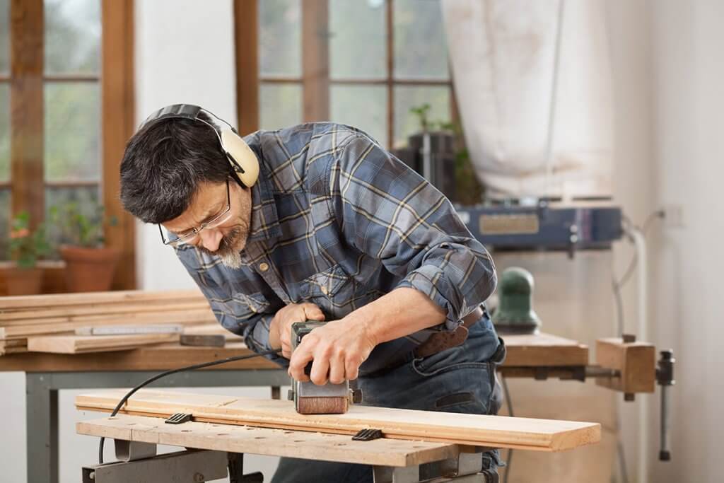 Person schleift Holz mit Bandschleifer