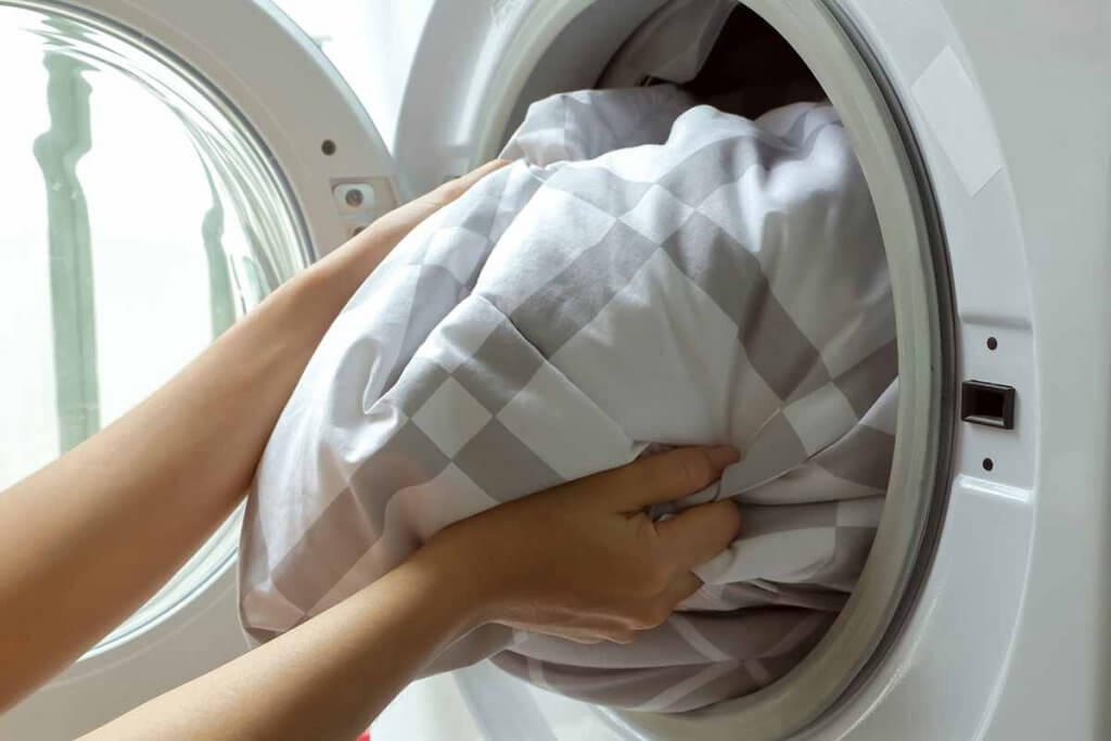 Person holt Bettdecke aus Waschmaschine