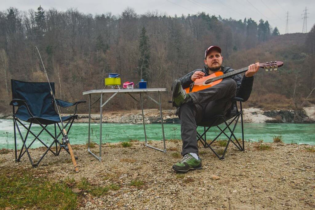 Mann sitzt auf Stuhl und spielt Gitarre. 