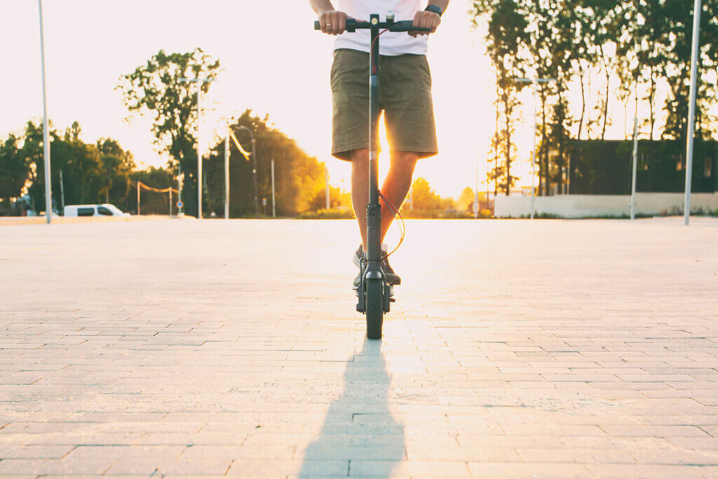person faehrt mit cityroller auf strasse der sonne entgegen