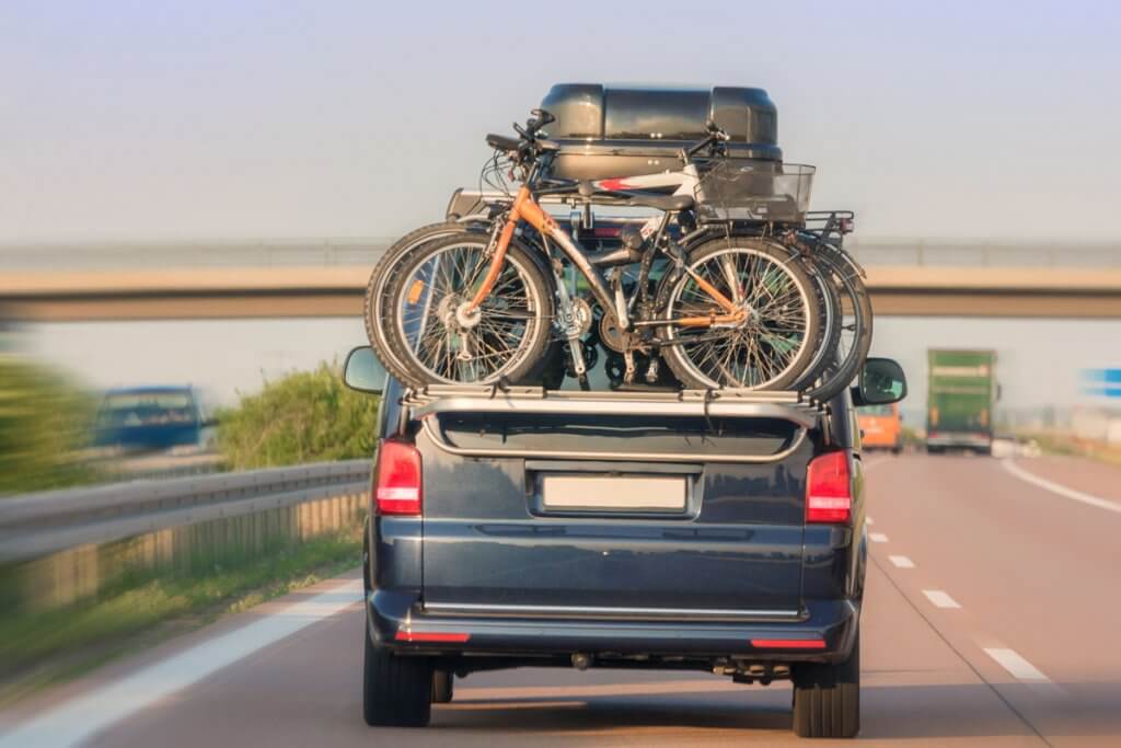 Ein mit Dachbox und Fahrraedern beladenes Auto fährt auf der Autobahn.