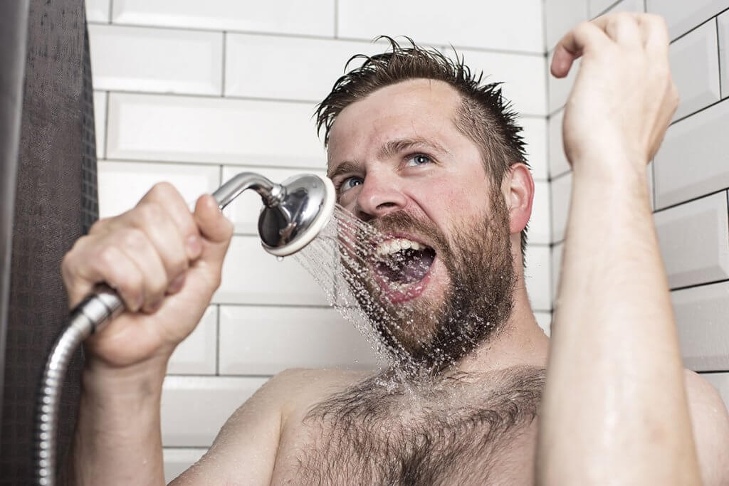 Mann singt in Dusche und nutzt Duschkopf als Mikrofon