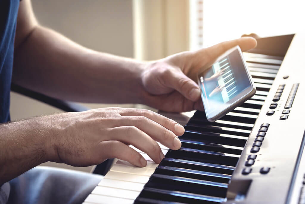 Mann am E-Piano mit Smartphone in der Hand