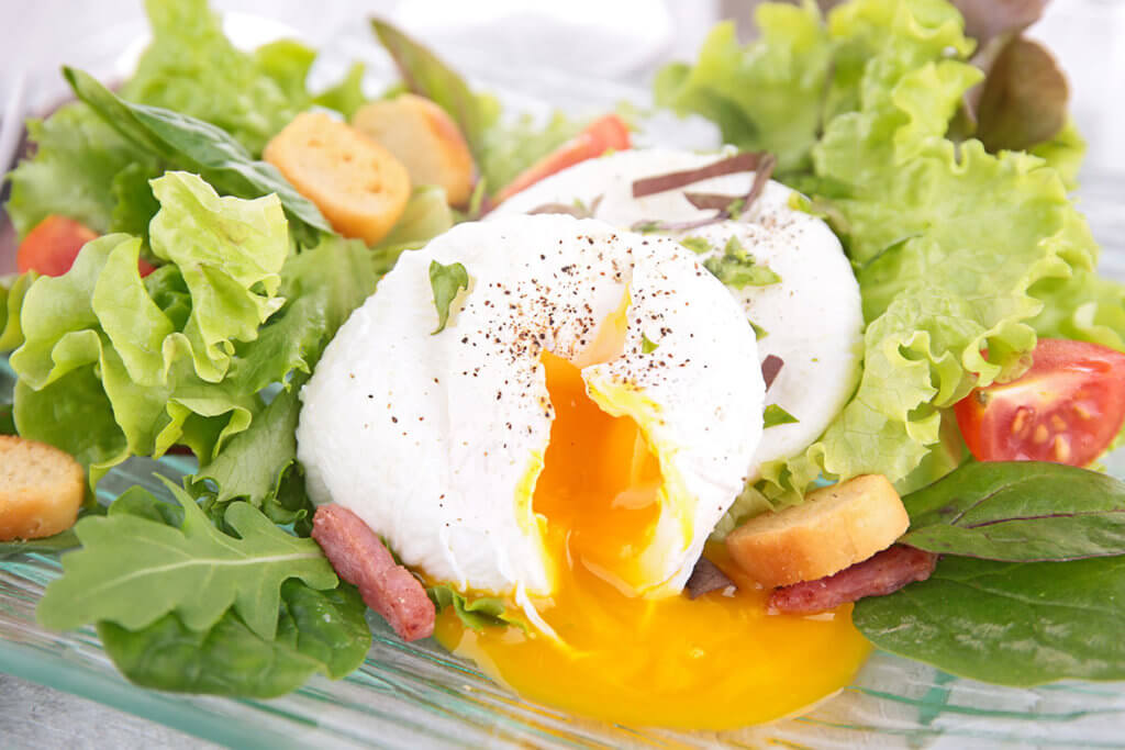 Fluessiges Eigelb fliesst aus einem Ei, das auf Salat liegt