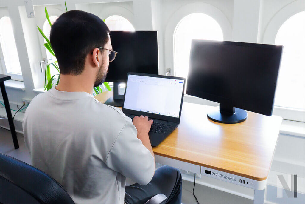 person sitzt am comhar und arbeitet mit laptop und zwei bildschirmen