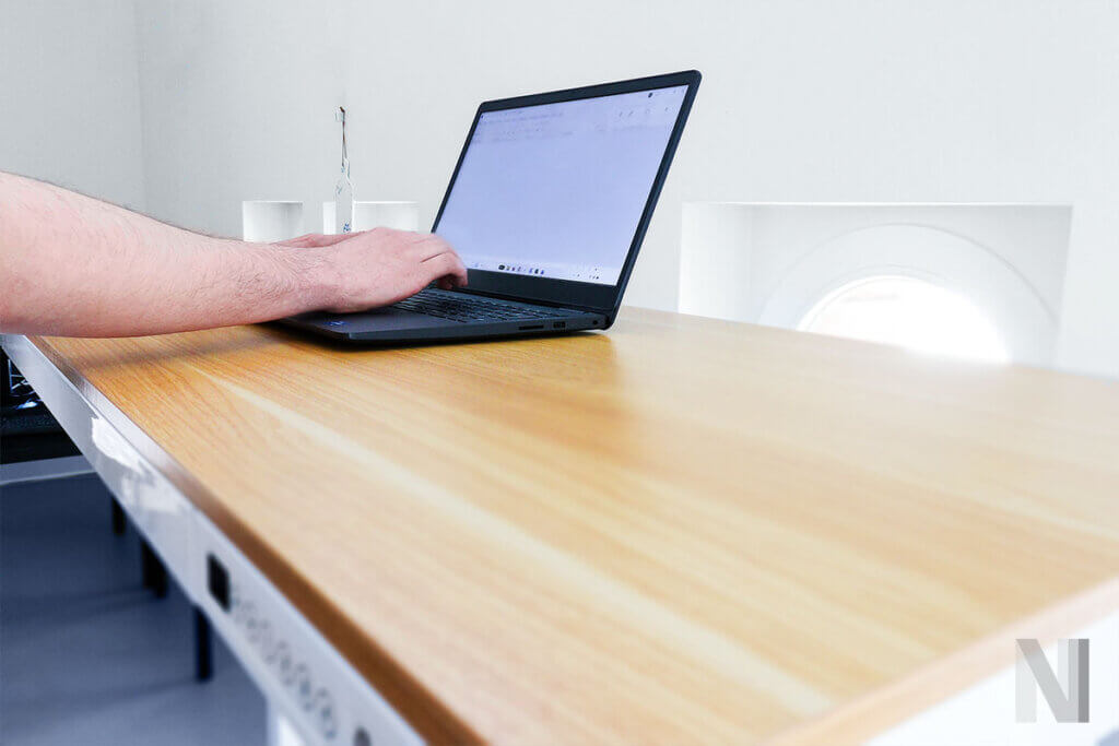 person tippt stehend am laptop, arme liegen nicht auf der tischplatte des comhar