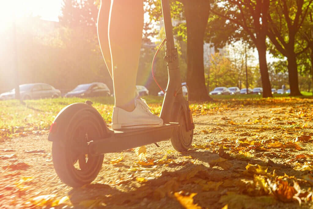 Person fährt mit Elektro-Scooter durch Herbstlaub