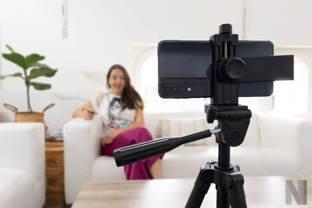 Person sitzt auf Sofa und macht Selfie mit Smartphone auf Stativ