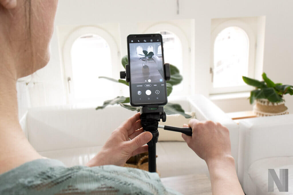Person stellt Smartphone auf Stativ ein