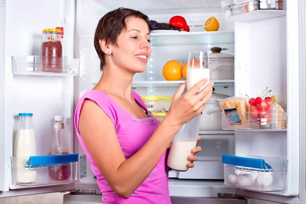 frau moechte milch aus einem glas vor offenem french door kuehlschrank trinken