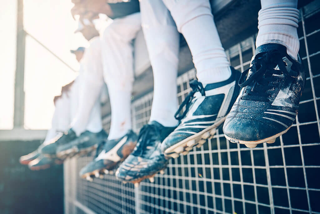 fussballschuhe-mehrere_personen_sitzen_auf_zaun_zeigen_schuhe