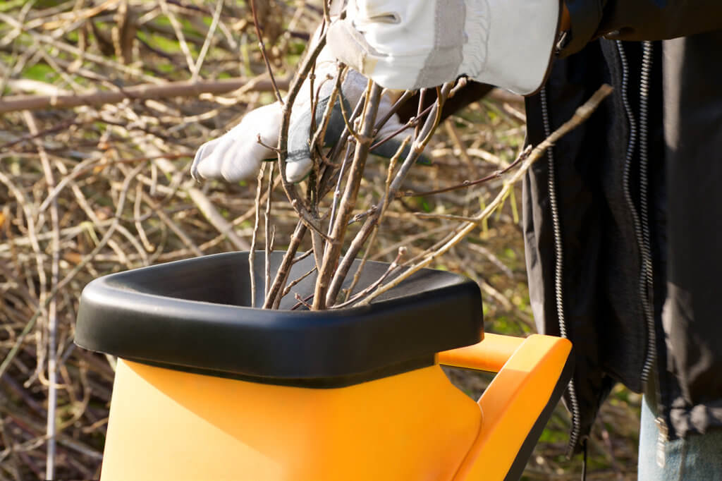 Aeste werden in einen Gartenhaecksler gelegt.