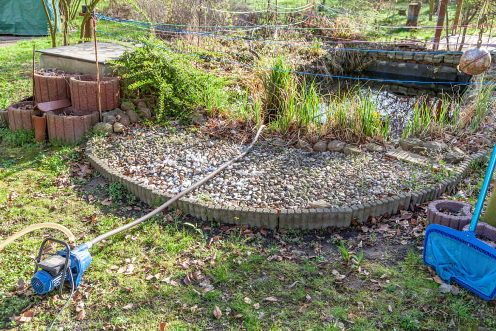 Eine Gartenpumpe saugt Wasser aus einem Gartenteich heraus