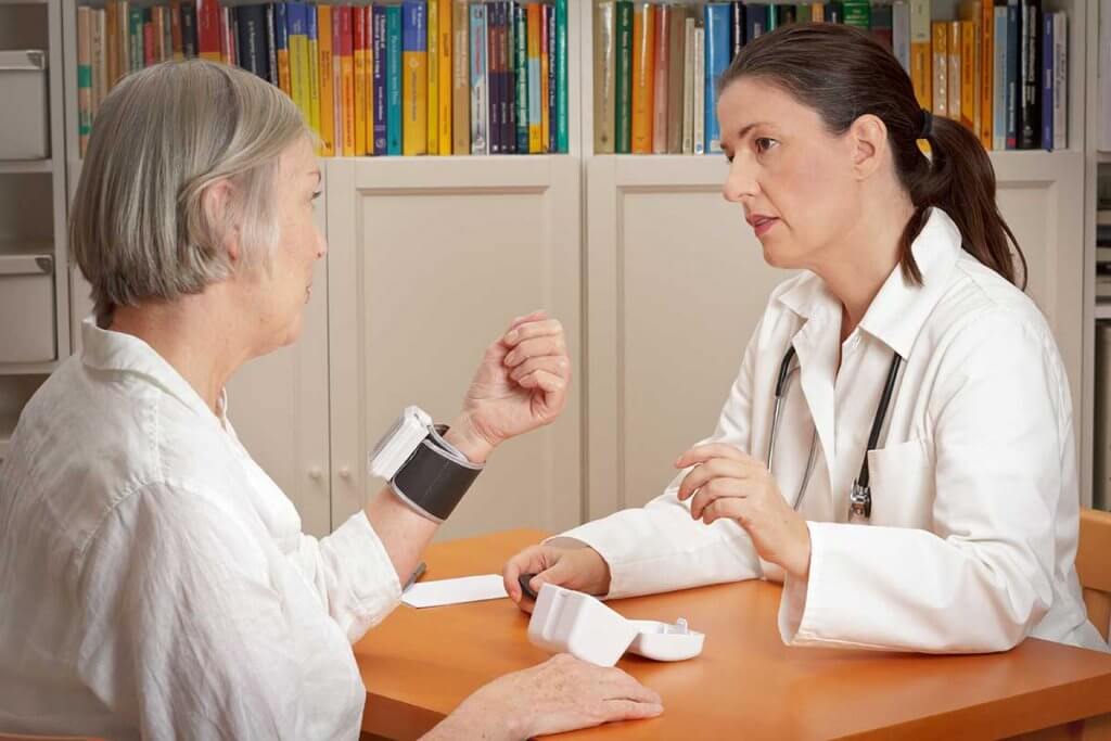Ärztin redet mit Patientin mit Blutdruckmessgerät am Handgelenk