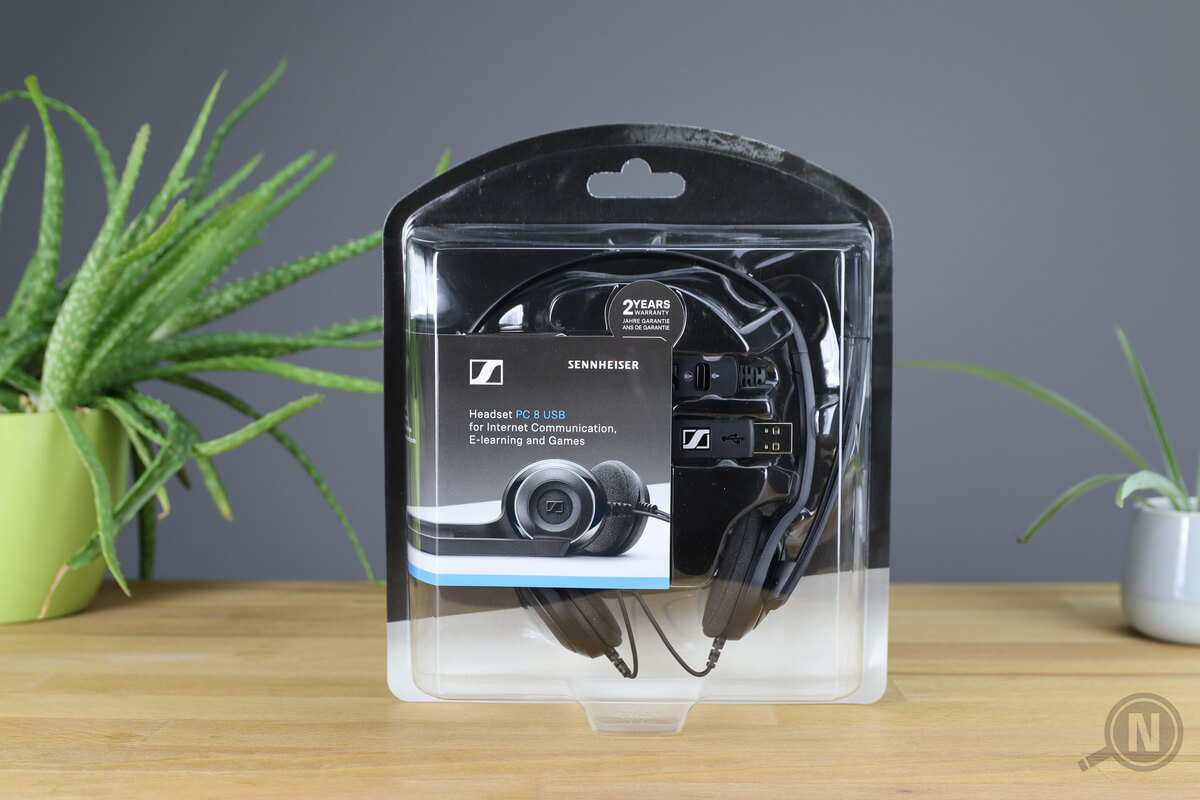 Headset von Sennheiser in transparenter Kunststoffverpackung zwischen zwei Pflanzen auf Holztisch