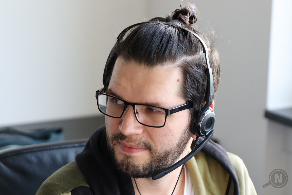 Halbprofil eines jungen Mannes mit Dreitagebart, Brille und am Hinterkopf zusammengeknoteten Haaren, der ein Headset trägt