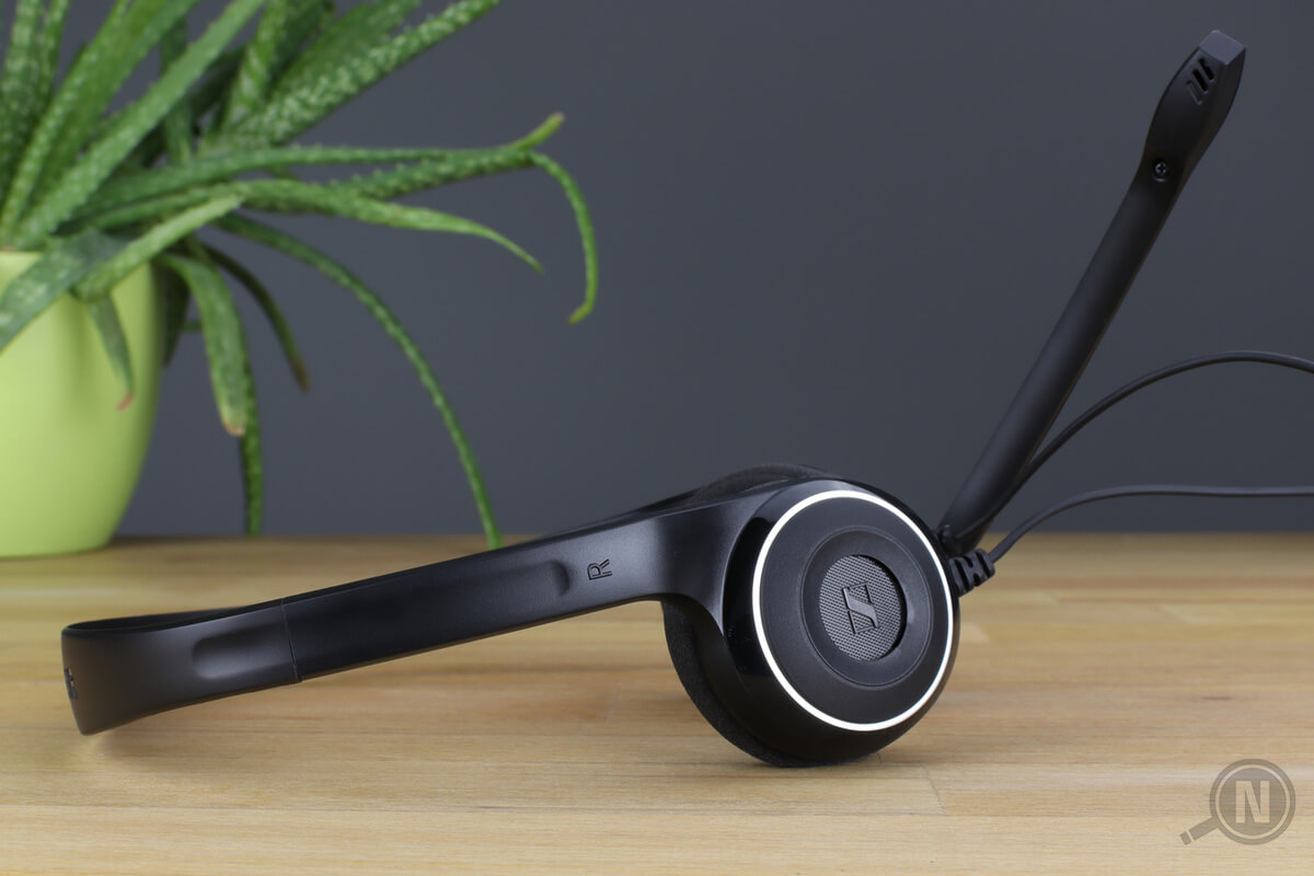 Schwarzes Headset auf Holztisch, Bügel zeigt nach links, Mikrofon nach rechts, links im Hintergrund steht eine Aloe-Vera-Pflanze
