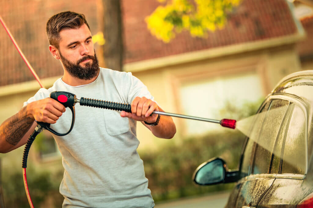 Mann reinigt Auto mit Hochdruckreiniger