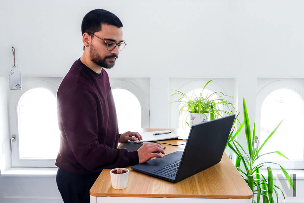 person arbeitet im stehen mit laptop an einem hoehenverstellbaren schreibtisch
