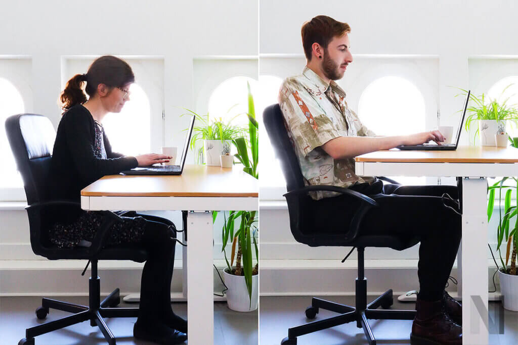 zwei personen arbeiten im sitzen an schriebtischen mit unterschiedlichen hoeheneinstellungen