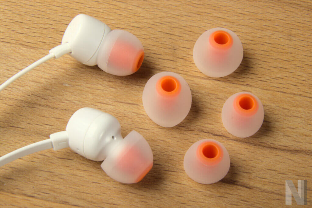Großaufnahme von weiß-orangen In-Ear-Kopfhörern mit zwei Paar Ersatz-Ohrstöpseln in verschiedenen Größen