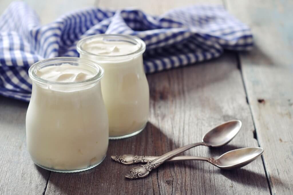 Griechischer Joghurt in zwei Glaesern mit zwei Loeffeln auf Holztisch