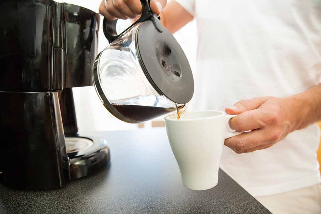 mann mit weissem shirt giesst kaffee aus glaskanne in eine weisse tasse