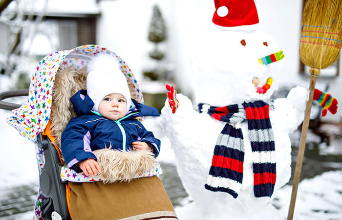 Baby in Kinderwagen neben Schneemann