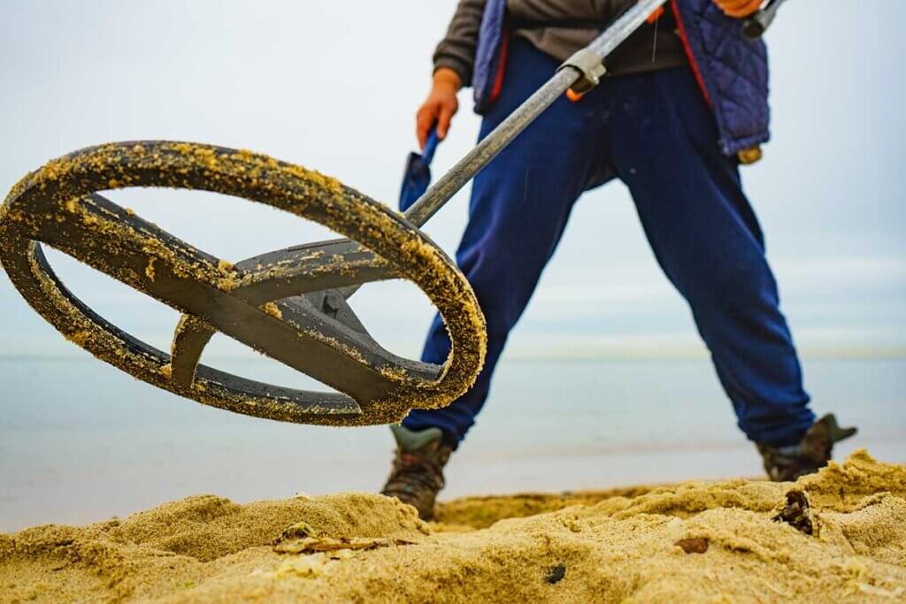 Mann steht mit Metalldetektor in Sand
