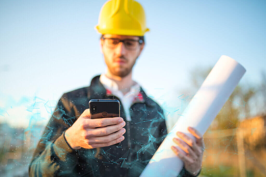 bauarbeiter mit schutzhelm hält ein outdoor-smartphone in der hand
