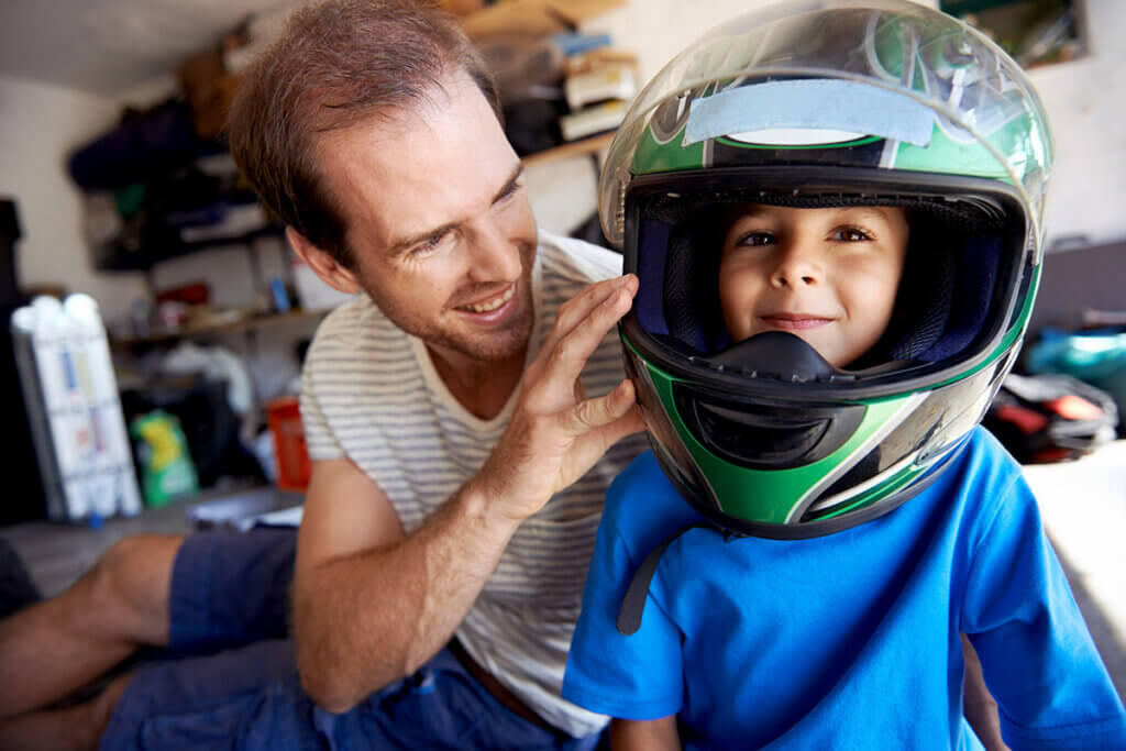 Junge trägt Motorradhelm mit Vater daneben