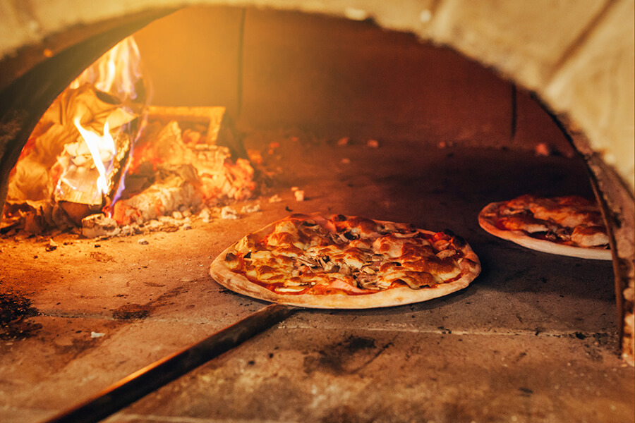 Aufnahme eines gemauerten Pizzaofens mit zwei Pizzen und einem Feuer