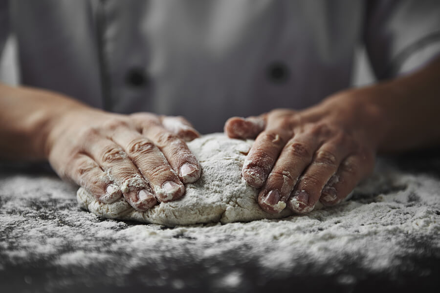 Person knetet einen Pizzateig 