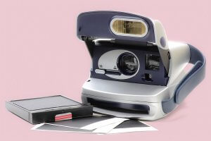 Eine Polaroidkamera in Nahaufnahme, daneben liegen eine Kassette und Bilder.