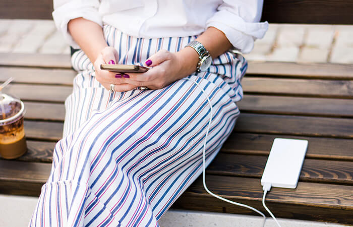 Frau sitzt mit Smartphone und Powerbank auf Parkbank