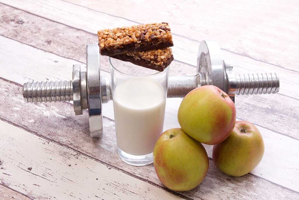 Proteinriegel neben Milchglas, Apfel und Hantel