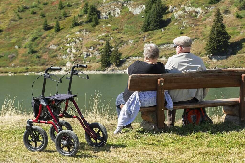 Senioren sitzen auf Bank am See mit Rollator daneben