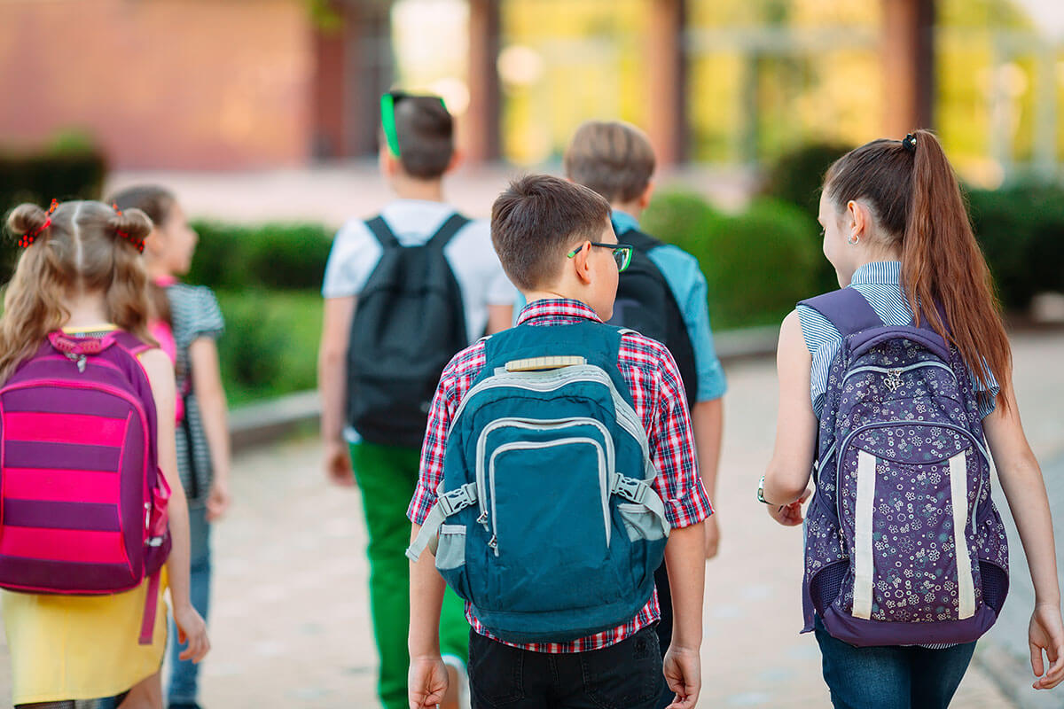 Gruppe von Schulkindern mit Rucksaecken auf dem Weg zur Schule