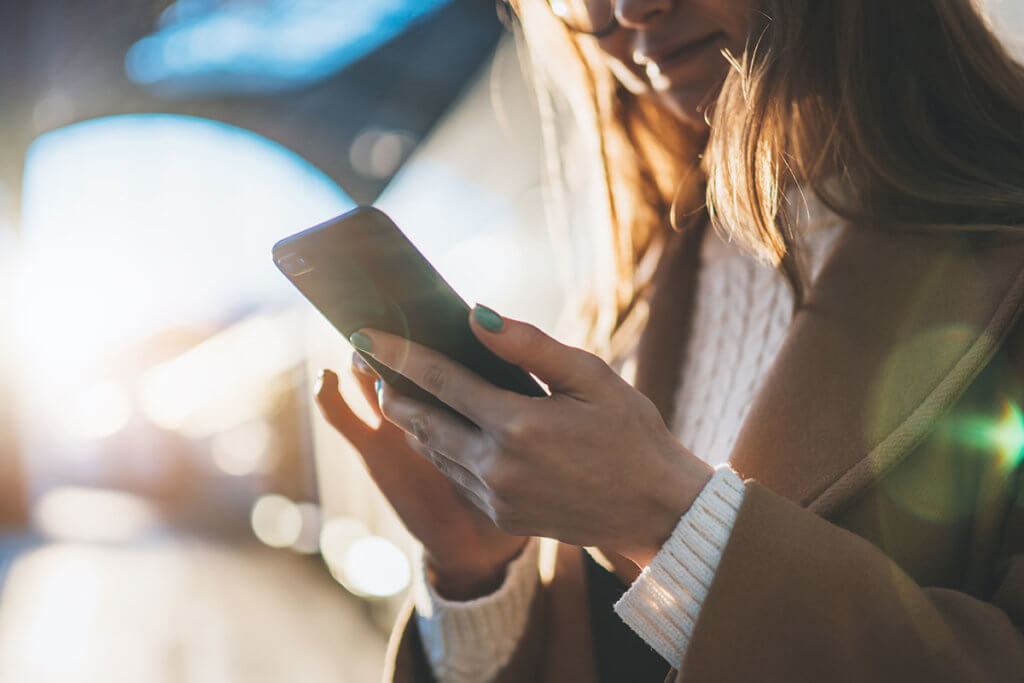 Frau haelt Smartphone am Bahnhof