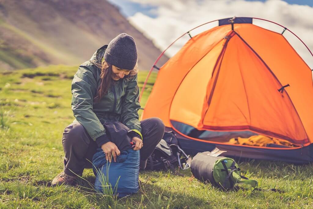 Person packt in einer Berglandschaft Schlafsack ein