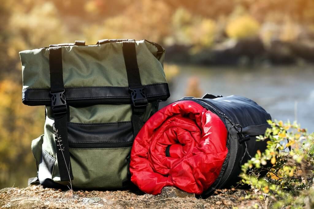 Rucksack steht neben eingerolltem Schlafsack in freier Natur